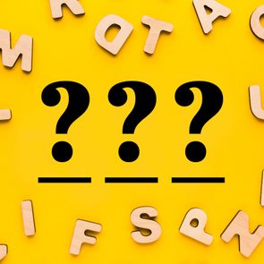 Wooden letters scattered on yellow background, surrounding three large black question marks in the center.