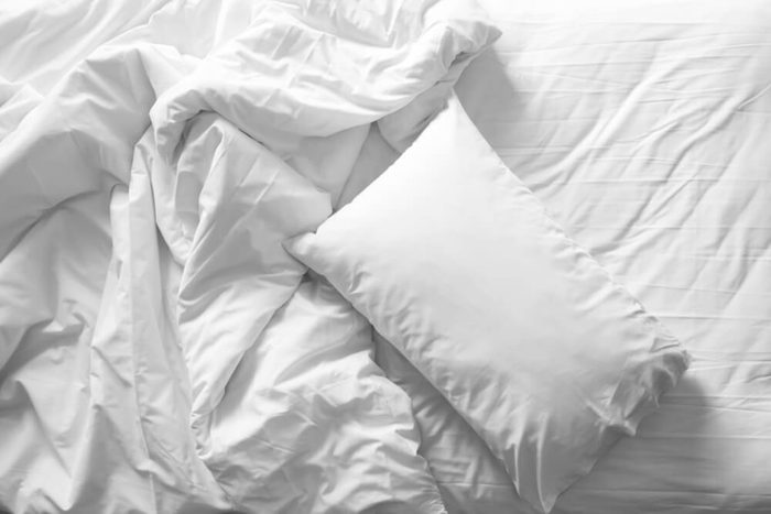 Messy bed. White pillow with blanket on bed unmade. Concept of relaxing after morning. With lighting window. Top view. Black and white theme.