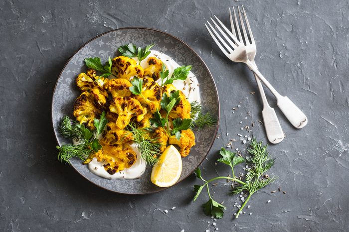 Roasted turmeric cauliflower with greek yogurt dressing. Delicious healthy snack on a dark background, top view 