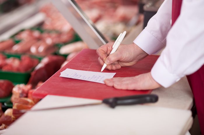 Butcher's hand writing on paper at counter in shop