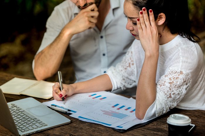 Young business woman writing details the graph with businessman, her has headaches on details on graph