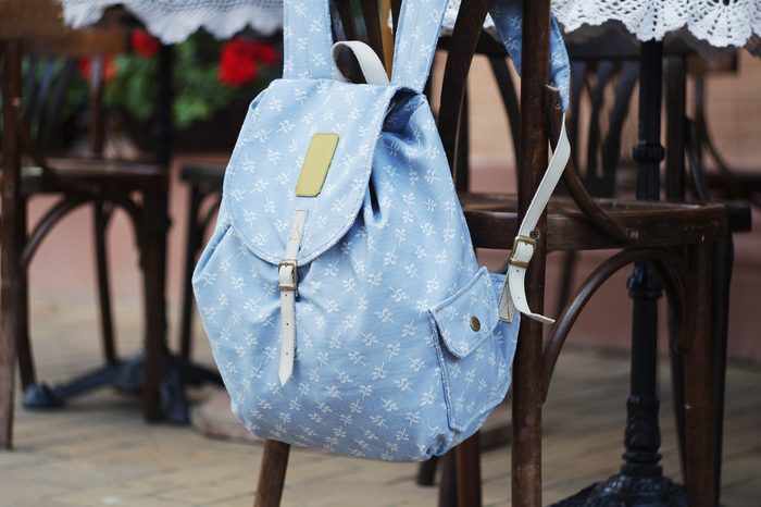 Backpack on the chair of cafe. Blue with brown and white pattern bag. Hand made backpack for travelers.