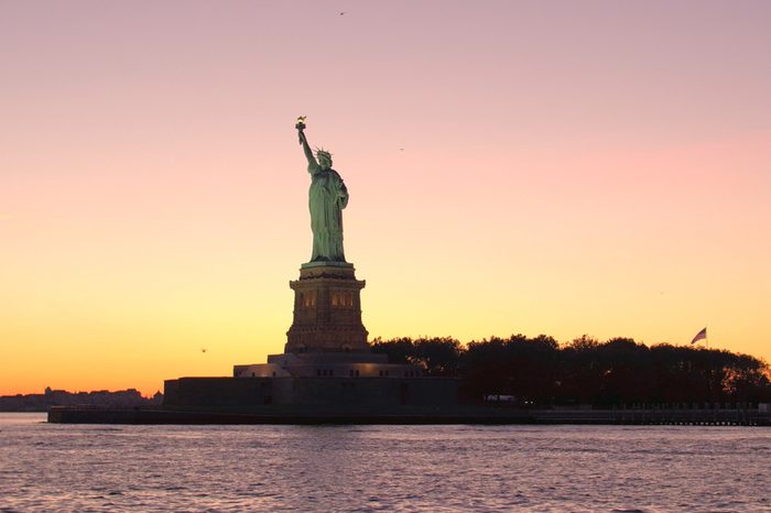 CLOSE UP LOW ANGLE VIEW Iconic Lady Liberty - the Statue of Liberty National Monument in New York Harbor against breathtaking golden sky at twilight. Famous copper sculpture resplendent in golden hues