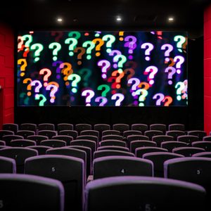 Question marks displayed on a large screen in an empty cinema, surrounded by red walls and numbered black seats.