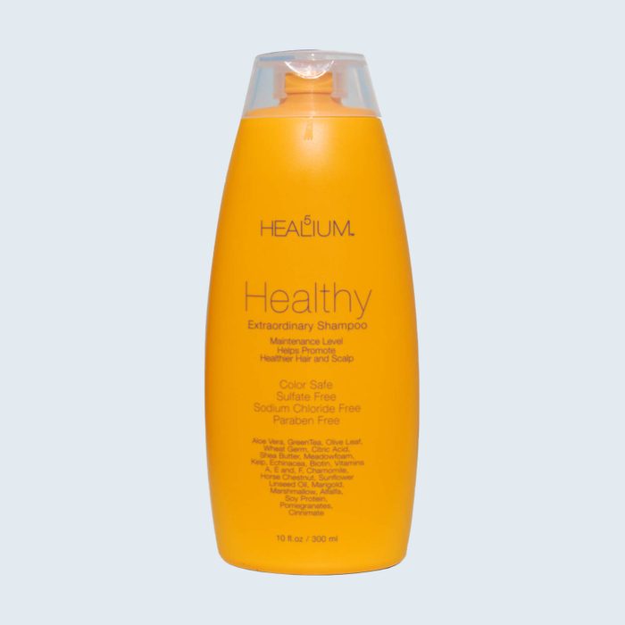 Orange shampoo bottle with text detailing brand and benefits, standing alone on a light background.