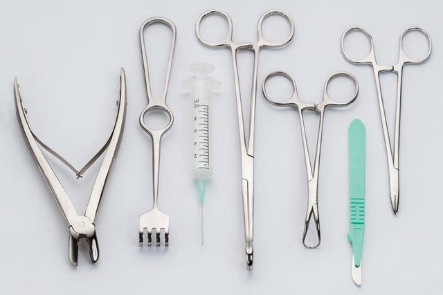 Surgical tools, including a syringe, scalpel, and forceps, are arranged side by side on a light gray background.