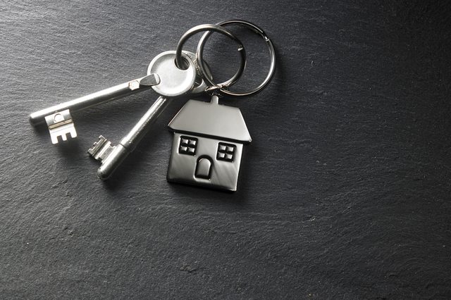 Keys on a ring with a house-shaped keychain rest on a dark, textured surface.