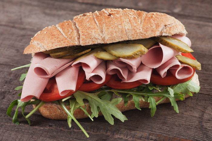 Submarine sandwich with bologna sausage, pickles, tomato and rocket salad