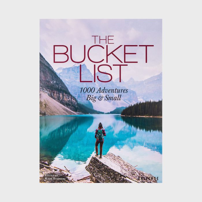Person stands on rock, overlooking a calm lake surrounded by mountains and forests. Text reads, 