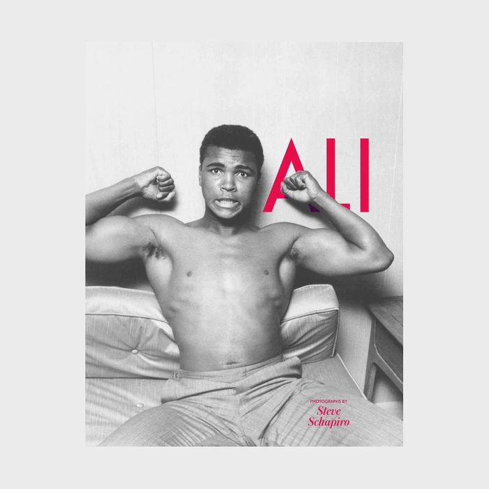 Shirtless man flexes biceps, sitting on a couch, expression playful; bold red text 