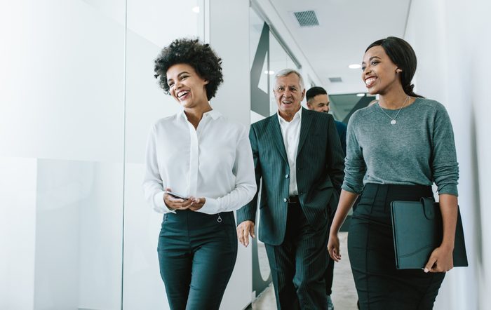 Diverse group of business people walking through office corridor. Team of corporate professionals walking and talking in modern office hallway.
