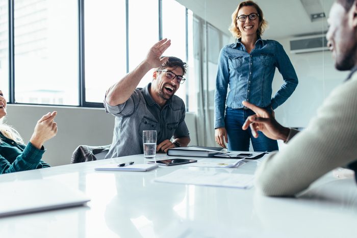 Businessman offering a high five to a coworker during a meeting in conference room. Positive boardroom environment.