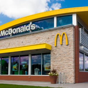 A McDonald's restaurant displays its logo and name on the building's exterior, surrounded by a clear sky and green landscaping.