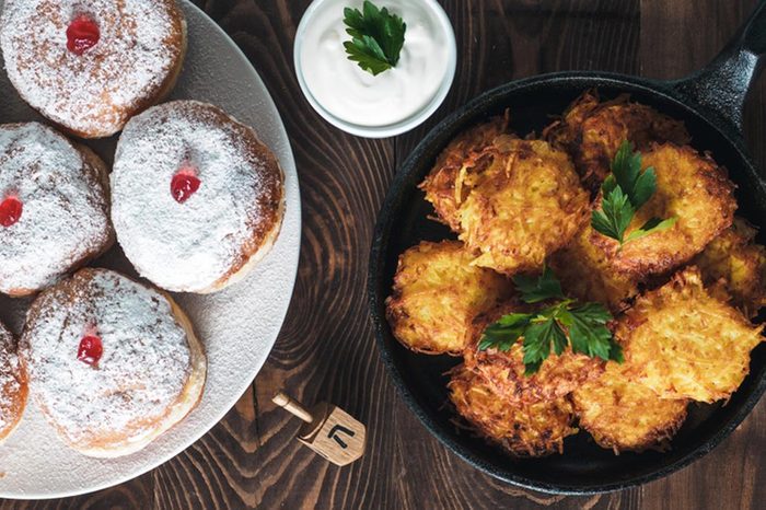 Jewish holiday Hanukkah concept and background. Hanukkah food doughnuts and potatoes pancakes latkes, oil and traditional spinnig dreidl on wooden table. Top view or flat lay. Copy space for text.