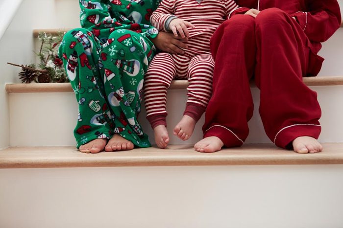 Three Children In Pajamas Sitting On Stairs At Christmas