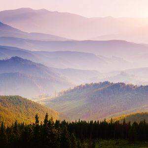Layers of misty mountains stretch into the distance, with sunlit valleys and dense forests creating a serene and expansive natural landscape.