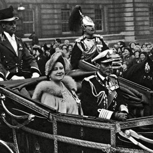A horse-drawn carriage carries elegantly dressed individuals, parading through a crowd-filled street with ornate buildings in the background.