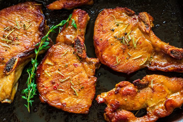 Roasted pork steaks, cutlets with bones and thyme on black baking sheet, top view.