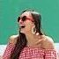 A woman laughs, wearing red sunglasses and striped off-the-shoulder top, against a bright green background.