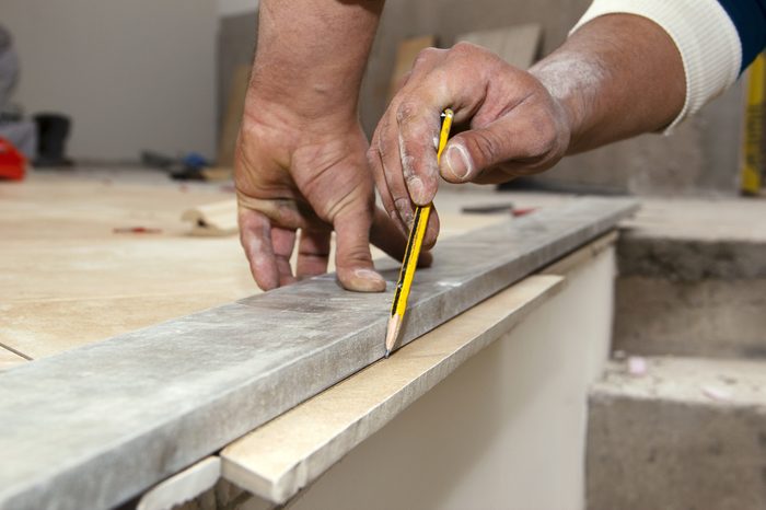 Laying ceramic floor tiles - man hands marking tile to be cut, closeup