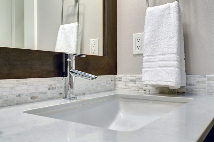Close-up view of bathroom vanity cabinet topped with white and grey counter paired with tile backsplash under framed mirror. Northwest, USA Northwest, USA