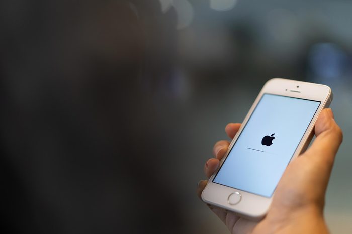 PHUKET, THAILAND - JAN 25, 2019: white apple iphone se with ios updated holding by right hand with blurred bokeh background, apple icon and status bar on screen