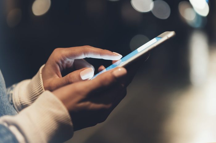 Girl pointing finger on screen smartphone on background illumination bokeh color light in night atmospheric city, hipster using in hands and texting mobile phone, mockup street, content lifestyle