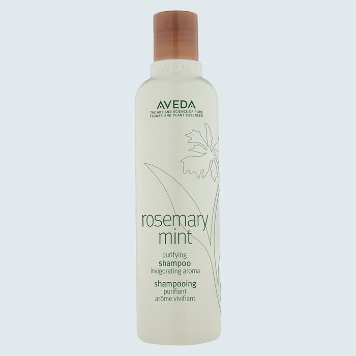 A bottle of Aveda rosemary mint shampoo stands upright against a plain background, labeled with floral illustrations.