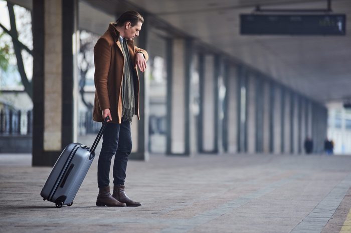 What time is it. Full length side view serious man looking at modern watch while keeping big suitcase. He waiting for train. Trip concept