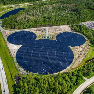 Solar panels form a Mickey Mouse shape; surrounded by greenery, parking lot, and roads in a landscaped area.