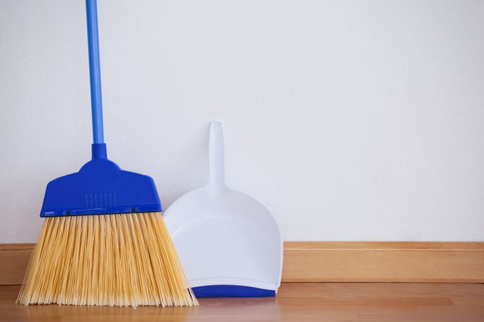 Close-up of dustpan and sweeping broom leaning against white wall