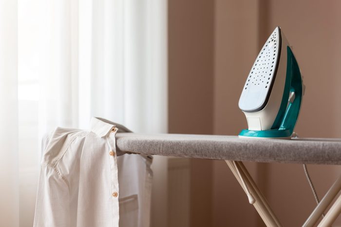 Ironed shirt hanging from an ironing board next to a hot iron. Selective focus on the iron