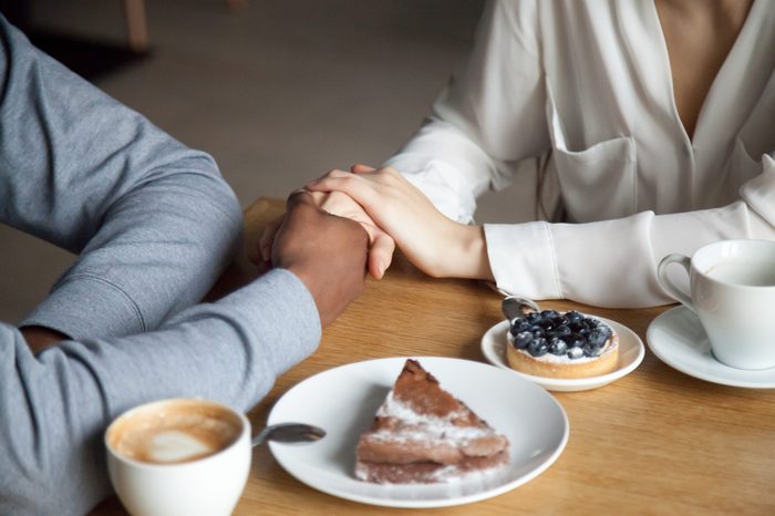 Interracial couple holding hands sit at cafe table, african black man and white woman in love enjoy date in coffee house concept, romantic biracial lovers meet in public place together, close up view