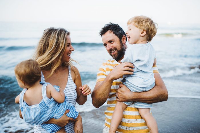 A young family with two toddler children standing on beach on summer holiday.