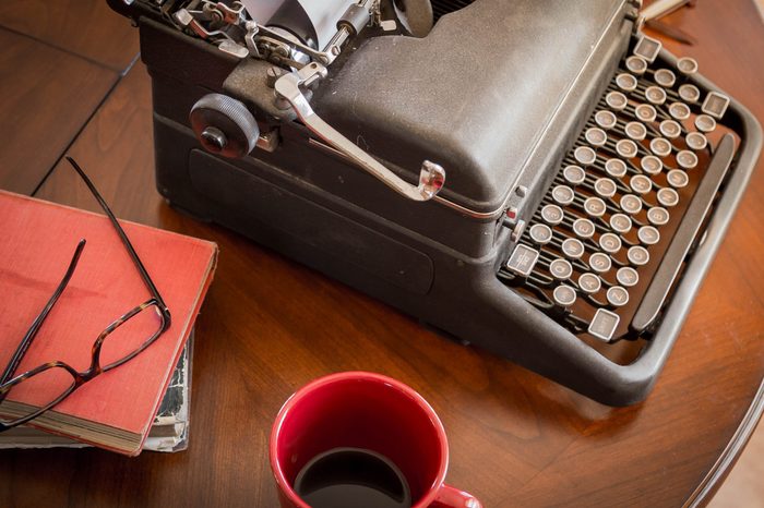 black retro typewriter sitting on wooden coffee table and cup of coffee, old worn books and stylish glasses are good for authors, writers, editors or journalists