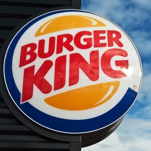 Burger King logo, displayed on a large circular sign, mounted outdoors beside a building, against a backdrop of a partly cloudy sky.