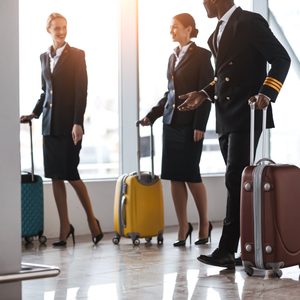 Airline crew walks with rolling suitcases in an airport terminal.