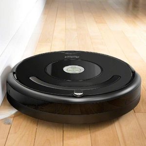 A black robotic vacuum cleans a wooden floor next to a white wall, displaying 