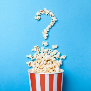 Popcorn spills from a striped bucket, forming a question mark shape against a blue background.