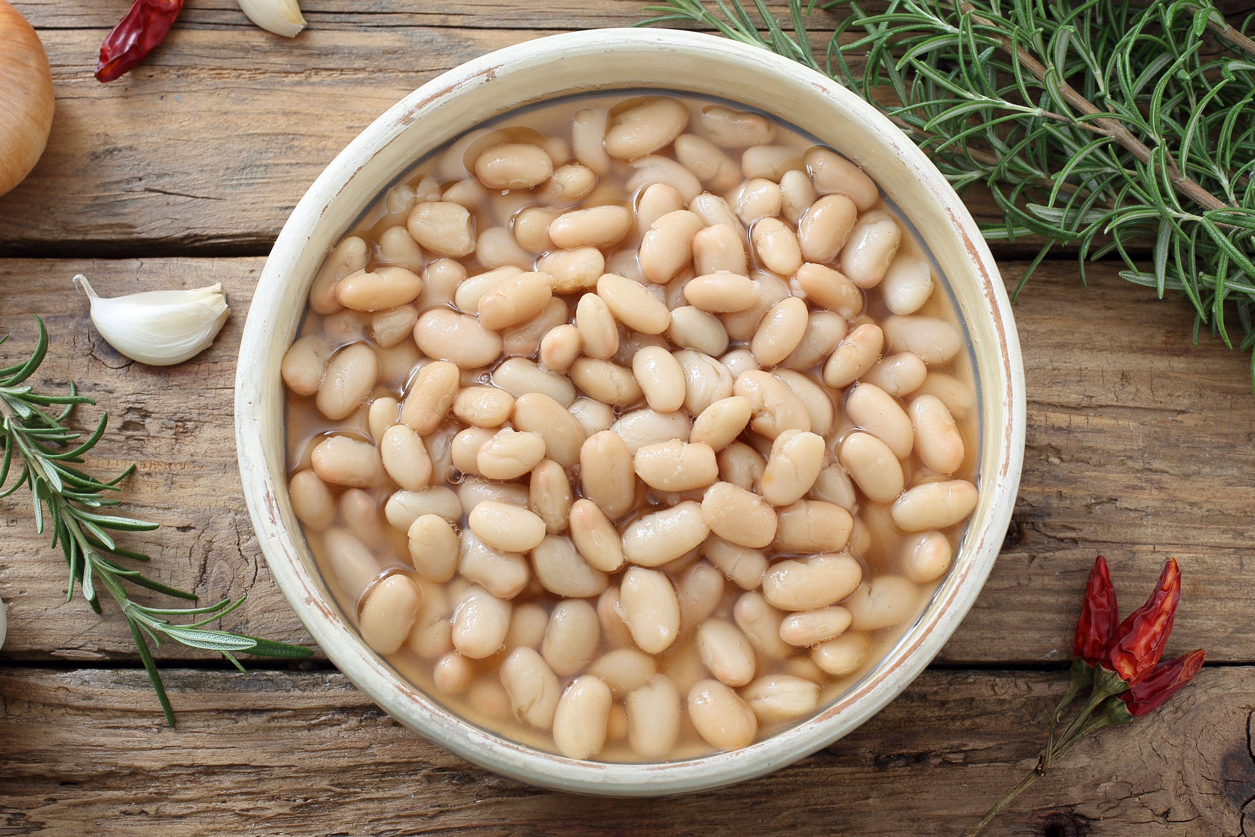 boiled white beans in ceramic bowl on a rustic chicken table background