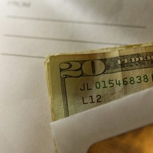 A $20 bill protrudes from an envelope, resting on a paper with 