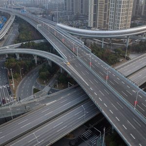 Elevated highways curve and intersect in a complex pattern amid urban high-rise buildings, with sparse vehicles.