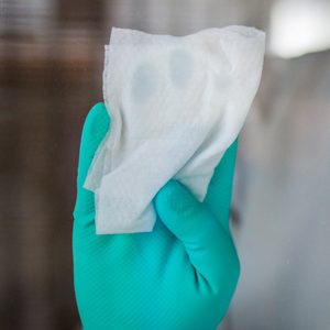 Gloved hand wipes a glass surface, creating a clean, streak-free area, with a blurred indoor background.
