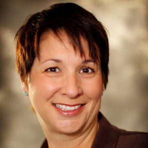 Smiling woman poses against a blurred, neutral-toned background.