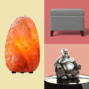 Salt lamp glowing on yellow background, gray ottoman resting on a red surface, and silver Buddha statue sitting on a reflective black base.