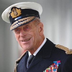 An elderly man in a naval uniform smiles, displaying military decorations, in a bright, indoor setting.