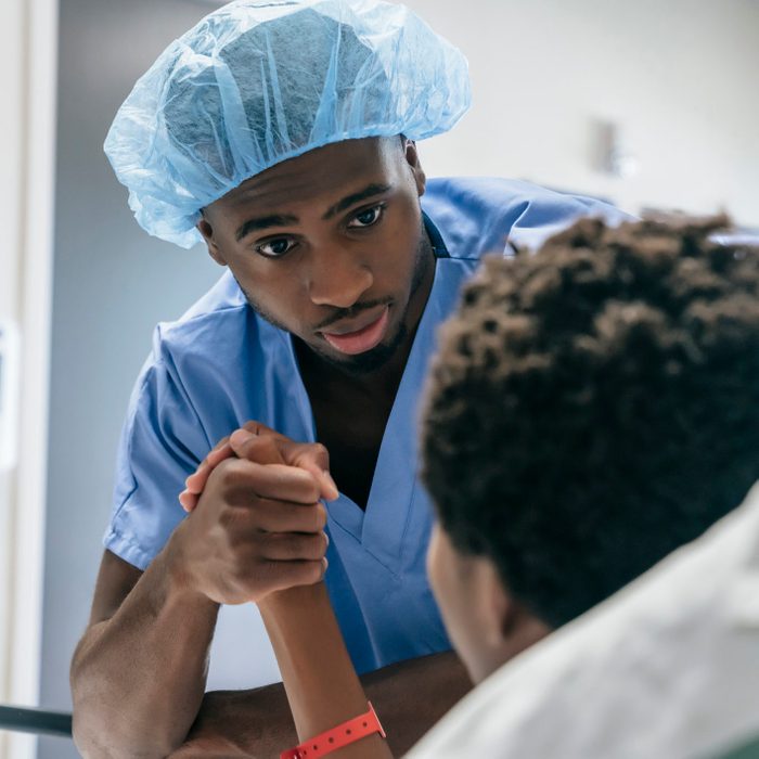 Black doctor holding hand of boy in hospital bed
