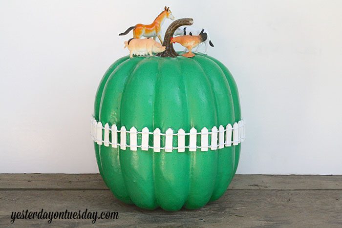 pumpkin painted green with a miniature white picket fence around it; plastic farm animals added on top