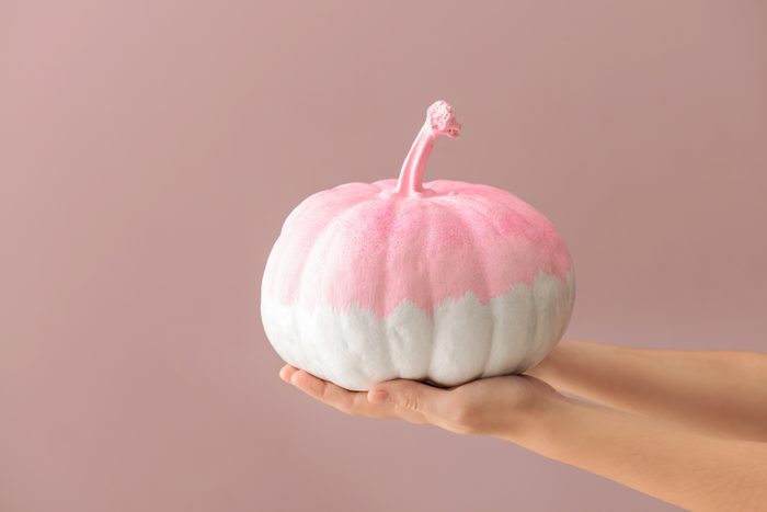 Woman holding painted pumpkin on color background