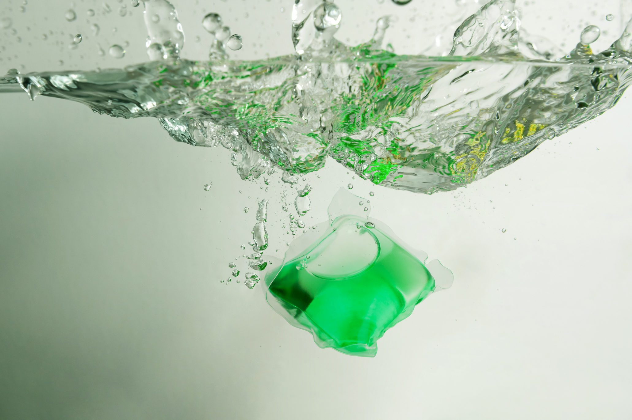 Green laundry detergent pod in water with splash.